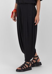 Svarta vida byxor med strukturerad yta, med en liten hjärtapplikation. Kombineras med svarta sandaletter med remmar och ett färgglatt armband.