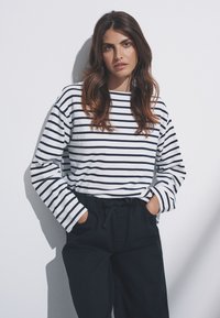 Top de manga larga en blanco con rayas azul marino, con un ajuste relajado y cuello redondo, combinado con pantalones oscuros.