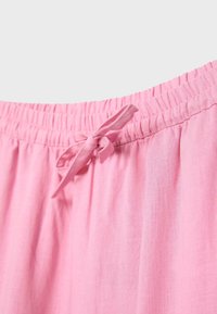 Taille élastique rose avec un cordon en tissu noué sur un pantalon ou un short léger et à texture douce.