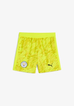 Neon sárga sportnadrág hullámos mintával, rugalmas derékpánttal, Manchester City logóval és fekete Puma logóval az oldalon.