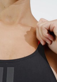 Černý plavecký top s kulatým výstřihem a designem s odhalenými rameny, s červenými akcenty a texturovaným vzorem na přední straně.
