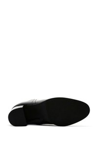 Black leather shoe with a flat sole, rounded toe, and stitched detailing. The textured rubber outsole provides grip and durability.