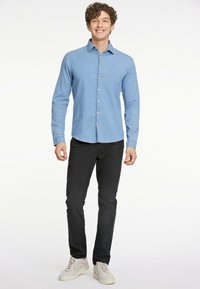 Vaaleansininen napitettava paita, joka on valmistettu denimistä, yhdistetty mustiin housuihin ja beigeihin sneaker-kengiin. Paidassa on kaulus ja pitkät hihat.