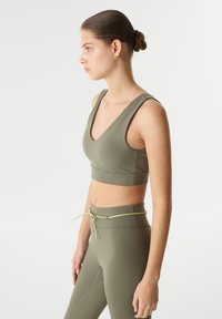 Olijfgroene sportbra met brede bandjes en een V-halsontwerp, gecombineerd met high-waisted leggings met een strikdetail in dezelfde kleur.