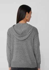 Sudadera gris con un acabado texturizado, que presenta una capucha con cordón, puños acanalados y dobladillo inferior, exhibida desde la parte posterior.
