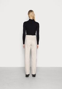 Suéter negro de canalé con cuello alto y pantalones de pierna ancha de color beige claro, posicionados frente a un fondo liso, con una textura suave y un minimalismo en los detalles.