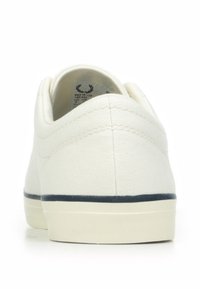 Sneaker bianco in tela con punta arrotondata, cuciture minime e un accento blu marino attorno alla suola. Il tallone presenta un colletto corto e imbottito.