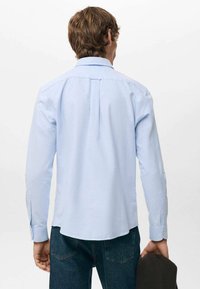 Jasnoniebieska koszula z długim rękawem o dopasowanym kroju, z zakładką z tyłu i zapinanymi na guziki mankietami, zestawiona z ciemnymi dżinsami i czarną kurtką.