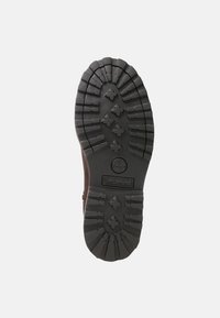 Suela de bota de goma con dibujos profundos para tracción, que presenta un logo circular y costillas prominentes sobre un fondo gris oscuro.