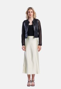 Černá kožená bomber bunda s průhlednými rukávy, zkombinovaná s krémovou saténovou midi sukni a černými sandály na podpatku. Jednoduchý, moderní design.