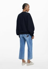 Navyfarbener Oversize-Sweatshirt mit herunterhängenden Schultern, kombiniert mit hellblauen, cropped Jeans, die mit einem bunten Patch auf der Hintertasche verziert sind.