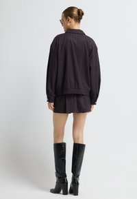 Donkerpaars pinstripe jack met een ontspannen pasvorm en een elastische tailleband, gecombineerd met een bijpassende korte rok en kniehoge zwarte laarzen met krokodilstructuur.