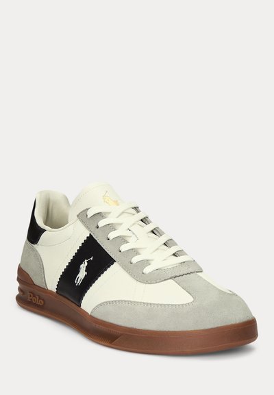 Pantof sport alb și gri cu dungă laterală neagră, talpă maro, șireturi albe și logo Polo care înfățișează un cal și un călăreț pe lateral și pe limbă.