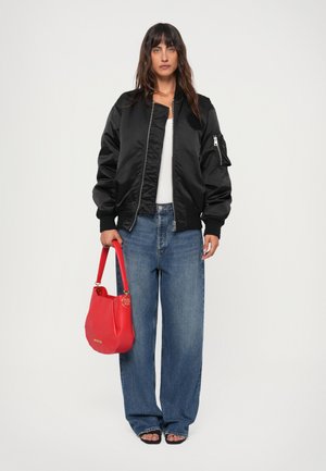 Black bomber jacket with a zip front, ribbed cuffs, and a side pocket, paired with wide-leg jeans and a red handbag with a gold accent.