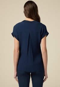 Marineblauwe blouse met korte mouwen, voorzien van een plooidetail aan de achterkant en opgerolde mouwen, gemaakt van een gladde stof.