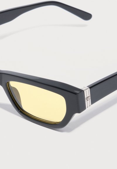 Μαύρα ορθογώνια γυαλιά ηλίου με παχιά σκελετό και κίτρινους φακούς, με ασημένια διακοσμητική λεπτομέρεια μεντεσέ.