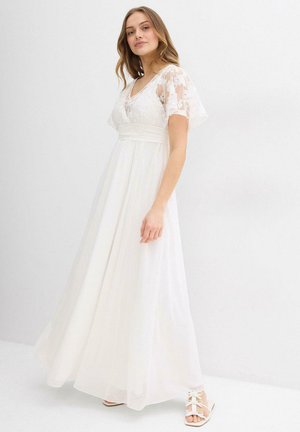 Abito maxi bianco con scollatura a V e maniche corte floreali trasparenti. Presenta una vita aderente e una gonna fluida, completato da sandali bianchi.