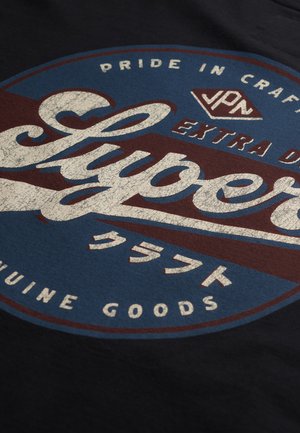 Granatowa koszulka z okrągłym logo, zawierającym biały i czerwony tekst. Wzór obejmuje teksturowany motyw oraz japońskie znaki na niebieskim tle.