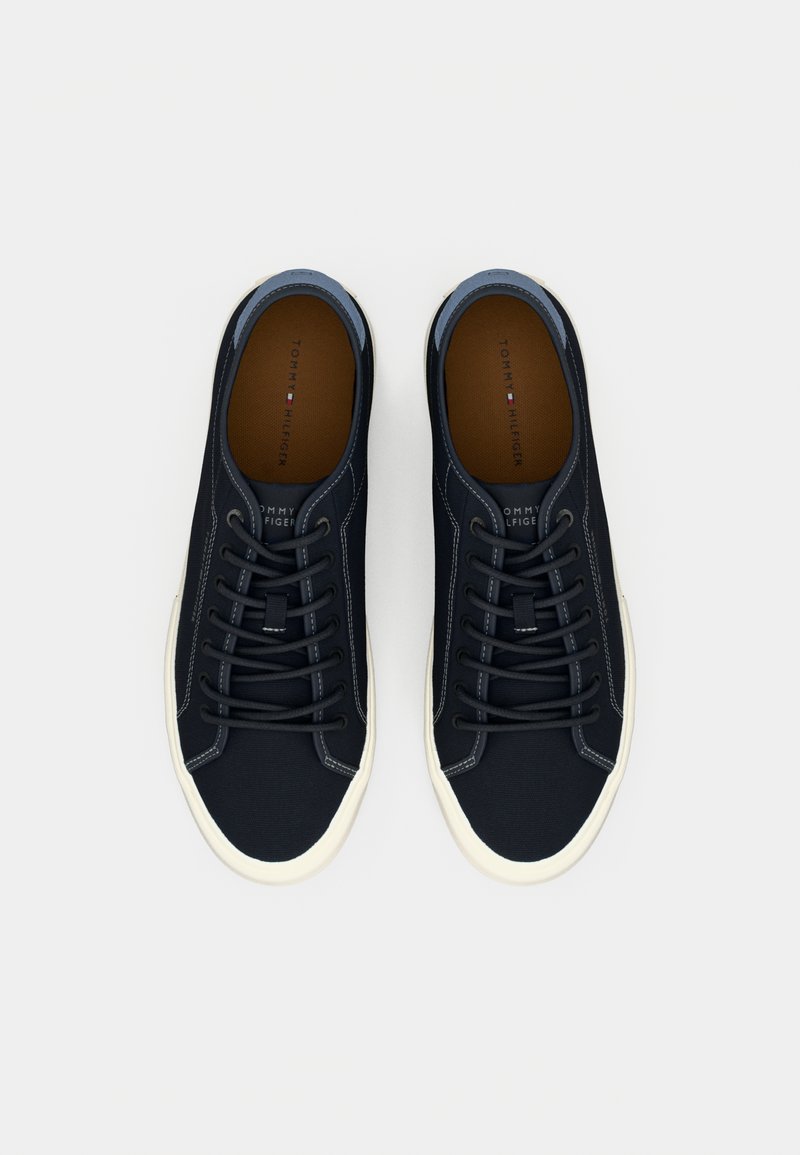 Baskets en toile bleu marine avec bout rond, semelle en caoutchouc blanche et lacets contrastés. L'intérieur présente une semelle intérieure beige avec un détail de marque.