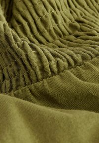 Tissu vert avec une section élastique froncée et plissée créant des plis verticaux texturés et une partie inférieure lisse.