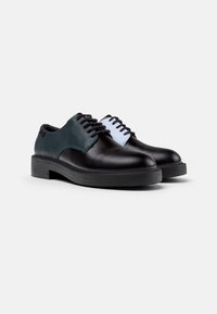Schwarze und grüne Lederschuhe mit kontrastierendem weißen Schnürpaneel, flacher Gummisohle, runder Zehenform und traditionellem Schnürdesign.