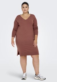 Rustkleurige gebreide jurk met een V-hals, lange mouwen, zijsplitten en een aansluitende jurk, gecombineerd met witte sportschoenen.