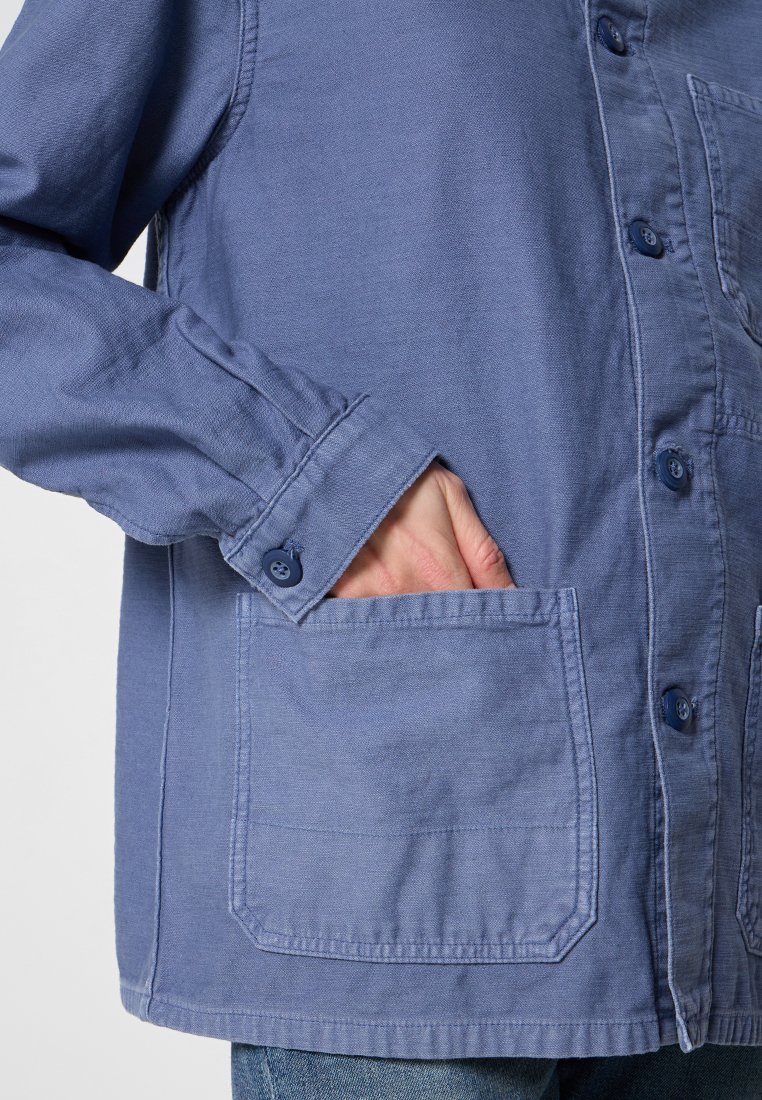 Blaue Baumwoll-Übergangsjacke mit Knopfleiste, langen Ärmeln und einer aufgesetzten Tasche in der Taille. Strukturierter Stoff mit einem lässigen Design.