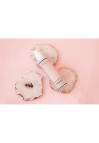 Rosa flaska med vit pump, märkt "Renaissance Body Treatment Milk", placerad på två cirkulära träskivor mot en rosa bakgrund.