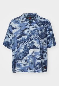 Camicia a maniche corte con bottoni in tessuto blu, caratterizzata da una stampa di scene tropicali con palme e velieri, con il marchio "Tommy Jeans" in bianco.