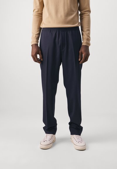 Mørkeblå joggerbukser med elastisk talje og sidelommer, lavet af blødt materiale. Kombineret med lyse sneakers.