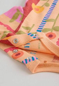 Prim-plan al unui material de culoare piersică cu imprimeuri florale și dungi, prezentând nasturi metalici cu capse de-a lungul marginii pentru fixare.