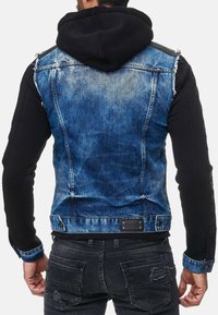 Denimjack met zwarte hoodie-mouwen, blauwe vervaagde wassing en versleten details. Bevat metalen hardware en een merketiket aan de achterkant.