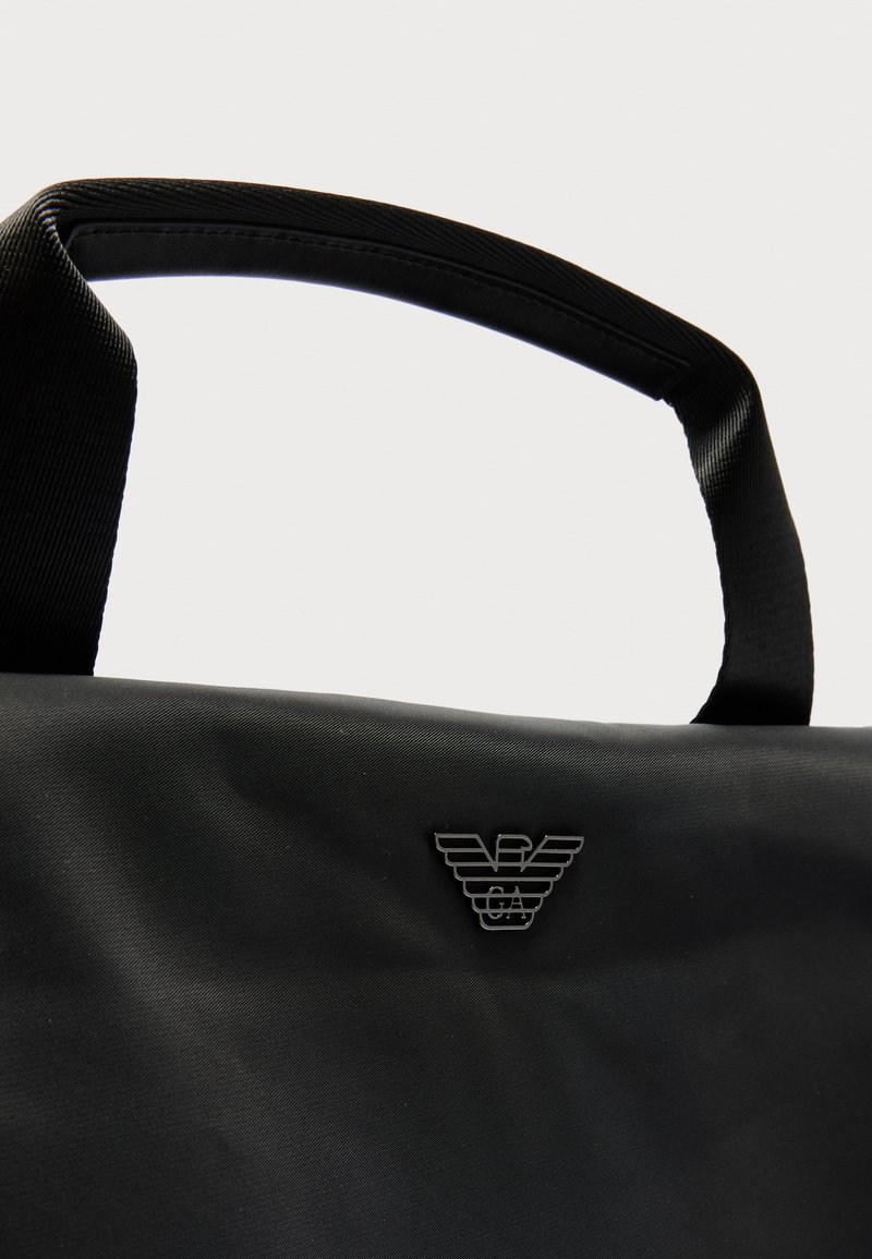Borsa tote in tessuto nero con manici testurizzati e un piccolo logo a forma di aquila metallica al centro anteriore.
