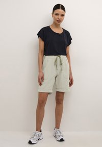 Camisa de manga corta azul marino con cuello redondo, combinada con pantalones cortos verdes claros hasta la rodilla y cintura con cordón, además de bolsillos laterales.