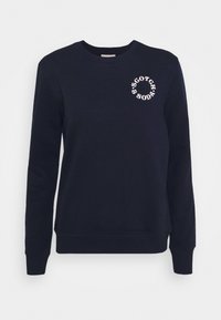 Laivastonsininen pitkähihainen collegepaita pyöreällä pääntiellä, jossa valkoiset pyöreät "Scotch & Soda" -tekstit vasemmassa ylärinnassa.