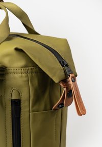 Borsa in tessuto verde oliva con cerniera nera e dettagli in pelle beige. Presenta una chiusura superiore a rotolo e una tasca laterale con cerniera.