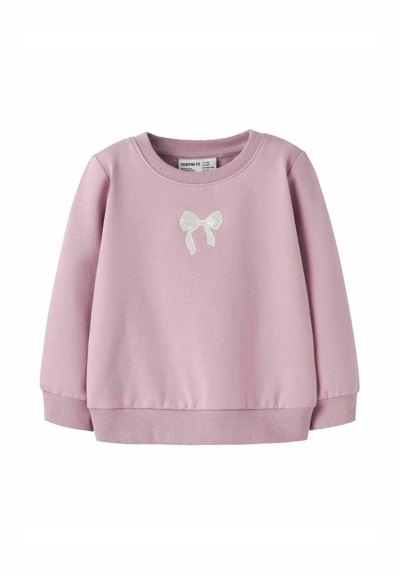 Sweatshirt rose clair avec un col rond, des poignets côtelés et un petit nœud blanc sur le devant. Fabriqué en tissu doux.