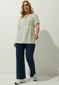 Vihreä ruudullinen pusero puffihuokosilla ja avonaisella kaula-aukolla, yhdistettynä tummansinisiin leveisiin farkkuihin ja valkoisiin lenkkareihin.