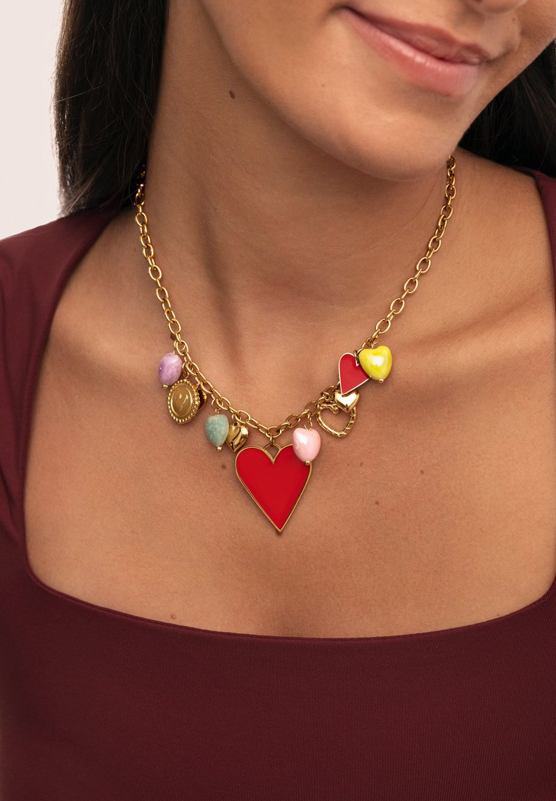 Collar de cadena de oro con un gran colgante en forma de corazón rojo, corazones de colores más pequeños en rosa, amarillo y verde, y otros charms decorativos.