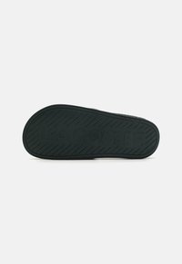 Semelle de sandale en caoutchouc noir avec un motif de grip texturé et le logo "LACOSTE" embossé sur toute la longueur. Forme plate et plus large pour plus de confort.