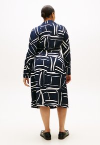 Φόρεμα σε ναυτικό μπλε με λευκό αφηρημένο μοτίβο, μακριά μανίκια, μανσέτες με κουμπιά και ζώνη στη μέση. Λείο ύφασμα με μήκος έως τη μέση του μηρού.