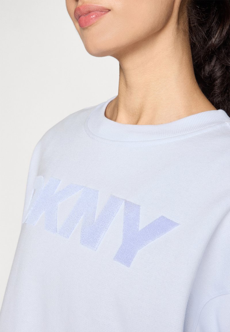 Jasnoniebieska bluza z teksturowanym, wypukłym logo "DKNY" w nieco ciemniejszym odcieniu. Klasyczny okrągły dekolt i miękka faktura materiału.
