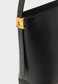 Zwarte lederen handtas met een gestructureerde afwerking, verstelbare riem en een gouden sluiting met een logodetail. Strak, modern ontwerp.