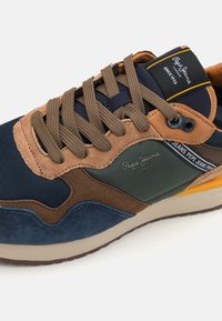 Multicolored sneaker featuring a mix of mesh and suede materials in navy, brown, green, and orange accents. Thick laces and logo detail visible.