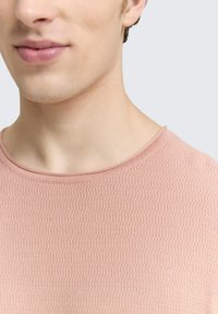 Lichtroze gestructureerde shirt met een ronde halslijn, met een verhoogd patroon en subtiele ribbels rond de kraag.