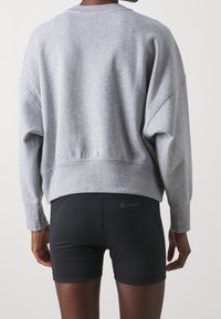 Grå, överdimensionerad sweatshirt med sänkt axel och ribbad fåll, kombinerad med svarta, figurnära shorts. Enkelt design med minimala detaljer.