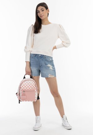 Maglione rosa pallido con maniche a palloncino, pantaloni corti in denim strappati e sneakers bianche. Zaino piccolo a scacchi con cerniera e tasca frontale.
