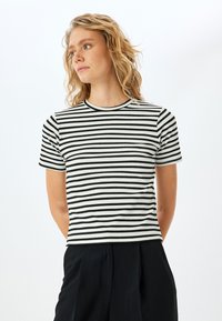 Camiseta de rayas en blanco y negro con cuello redondo y mangas cortas. Diseño ajustado con una tela texturizada.