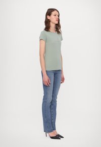 Lichtgroen strakke t-shirt met korte mouwen en een ronde hals; gecombineerd met blauwe rechte jeans en zwarte puntige hakken.