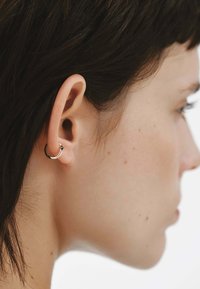 Pendiente de aro de plata con un pequeño acento de gema, colocado en una oreja perforada, mostrando una superficie suave y pulida y un diseño circular.